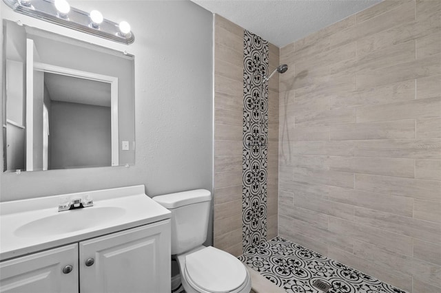 bathroom with tiled shower, vanity, a textured ceiling, and toilet