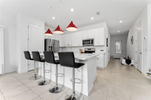 kitchen featuring a kitchen bar, stainless steel appliances, pendant lighting, white cabinetry, and an island with sink