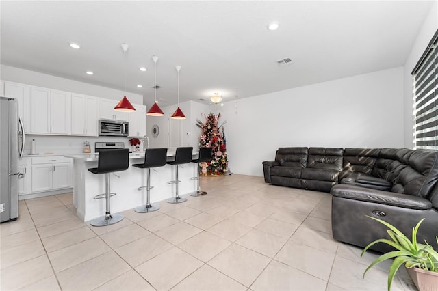 kitchen featuring white cabinetry, stainless steel appliances, pendant lighting, a kitchen bar, and a kitchen island with sink