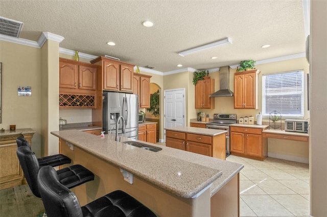 kitchen with stainless steel appliances, ornamental molding, a kitchen island with sink, and wall chimney range hood