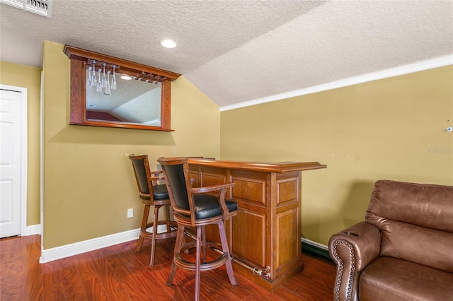 bar featuring vaulted ceiling, ornamental molding, dark hardwood / wood-style floors, and a textured ceiling