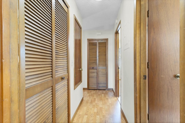 hallway with a textured ceiling and light wood-type flooring