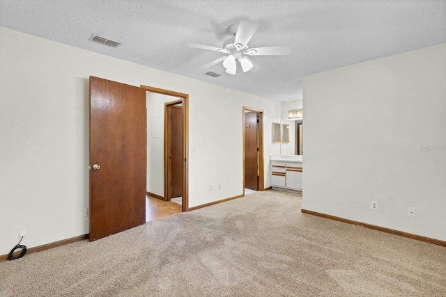 unfurnished bedroom with ceiling fan, ensuite bath, light colored carpet, and a textured ceiling