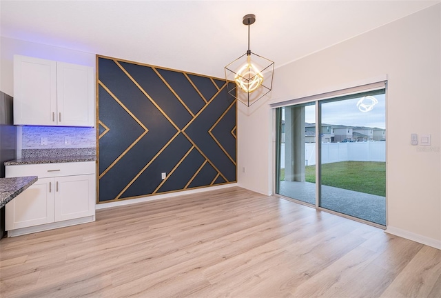 unfurnished dining area featuring an inviting chandelier and light hardwood / wood-style flooring