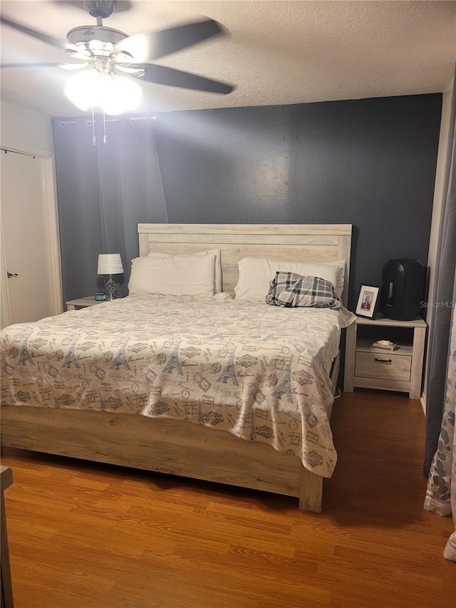 bedroom with ceiling fan, wood-type flooring, and a textured ceiling