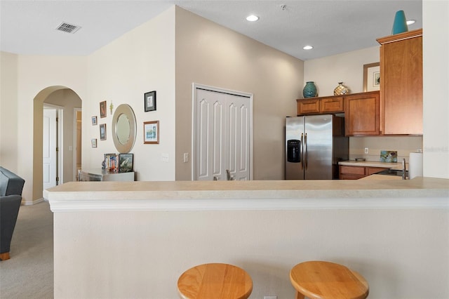 kitchen featuring a breakfast bar, stainless steel fridge with ice dispenser, sink, light colored carpet, and kitchen peninsula