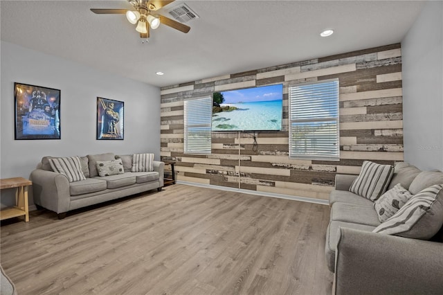 living room with ceiling fan, wooden walls, and light hardwood / wood-style floors