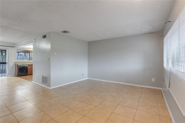 empty room with light tile patterned flooring, a textured ceiling, and wine cooler