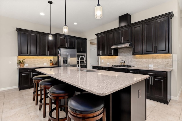 kitchen with gas cooktop, stainless steel refrigerator with ice dispenser, a kitchen island with sink, and decorative light fixtures