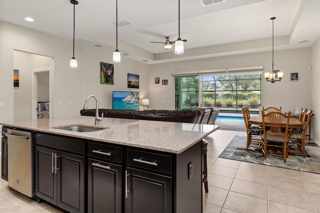 kitchen featuring stainless steel dishwasher, sink, light stone counters, and a center island with sink