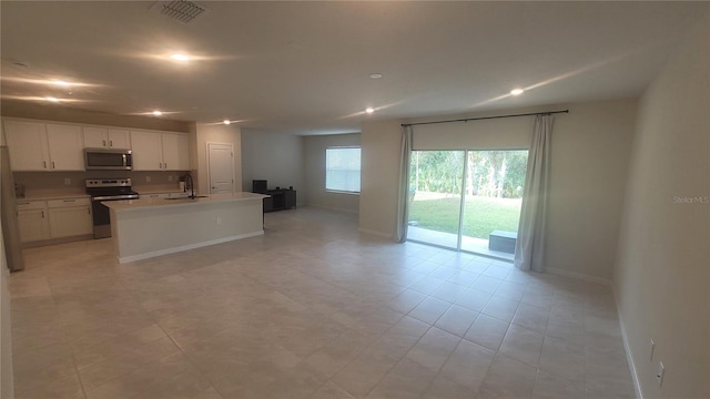 kitchen with stainless steel appliances, an island with sink, light tile patterned floors, white cabinetry, and sink