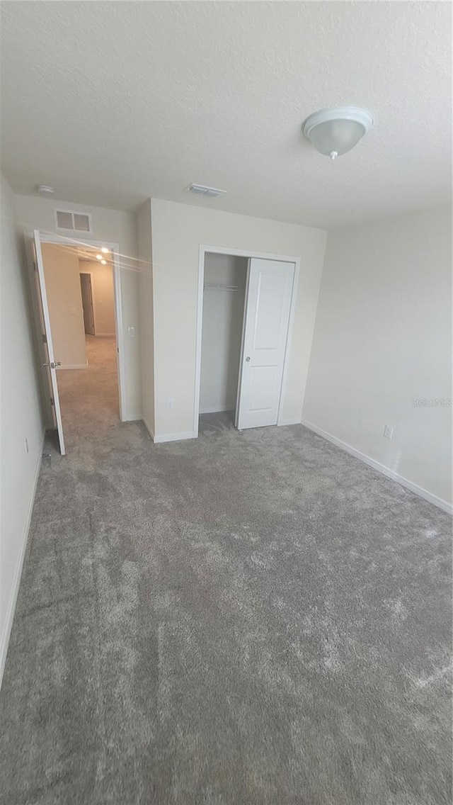 unfurnished bedroom featuring a textured ceiling, a closet, and dark colored carpet