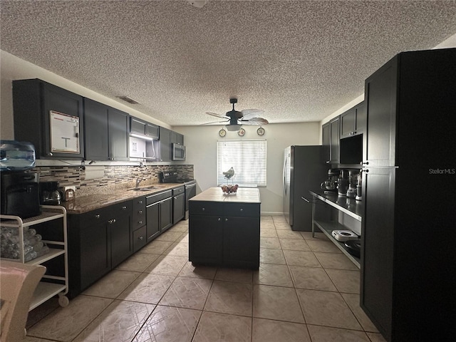 kitchen with a kitchen island, backsplash, light tile patterned floors, ceiling fan, and stainless steel appliances