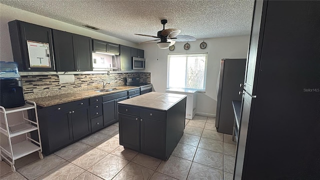 kitchen with sink, ceiling fan, appliances with stainless steel finishes, backsplash, and a kitchen island