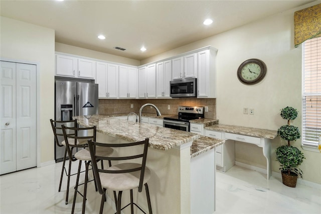 kitchen with stainless steel appliances, white cabinetry, a kitchen bar, an island with sink, and backsplash