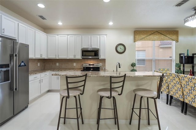 kitchen with a breakfast bar area, stainless steel appliances, light stone countertops, decorative backsplash, and white cabinetry