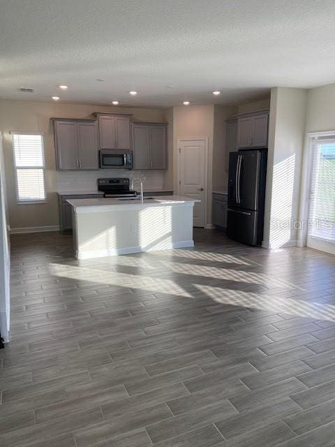 kitchen with black refrigerator, electric range oven, a center island with sink, and a healthy amount of sunlight