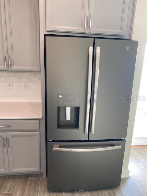 interior details with stainless steel refrigerator with ice dispenser, backsplash, gray cabinets, and light wood-type flooring