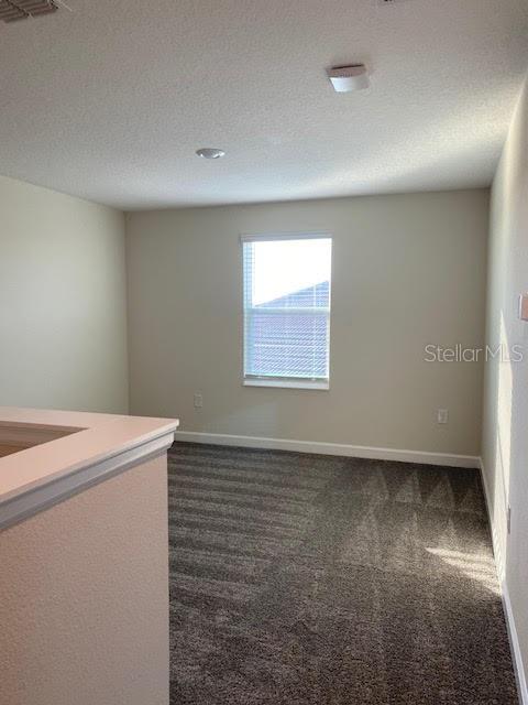 unfurnished room with a textured ceiling and dark colored carpet