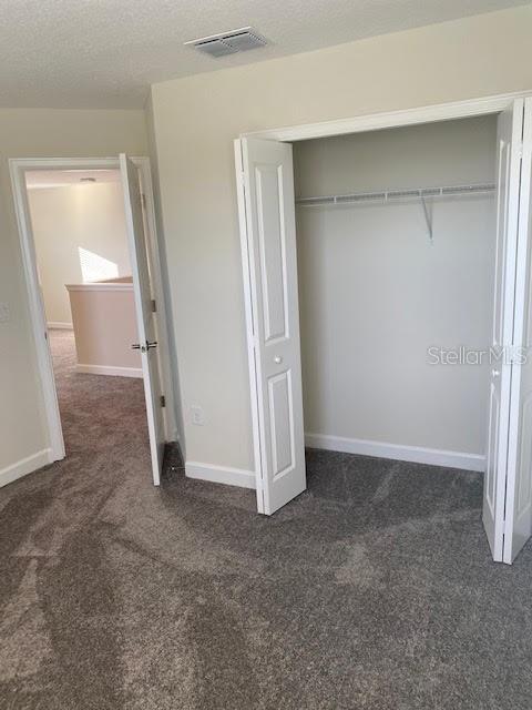 unfurnished bedroom featuring a textured ceiling, a closet, and dark colored carpet