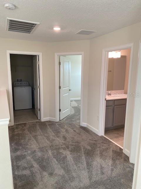 hall featuring dark carpet, a textured ceiling, and washer / clothes dryer