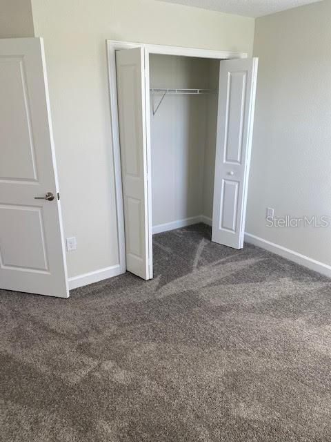 unfurnished bedroom with a textured ceiling, a closet, and dark carpet