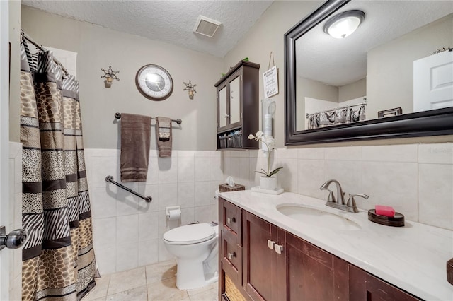 bathroom with a textured ceiling, tile patterned flooring, tile walls, toilet, and vanity