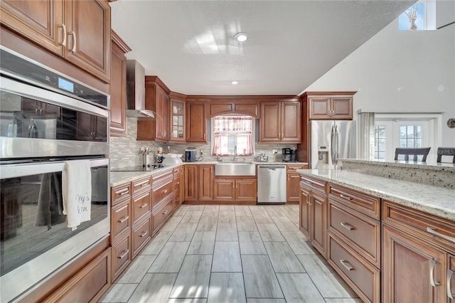 kitchen featuring appliances with stainless steel finishes, sink, light stone counters, and wall chimney exhaust hood