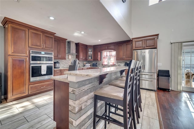 kitchen featuring appliances with stainless steel finishes, a wealth of natural light, light stone counters, and wall chimney exhaust hood