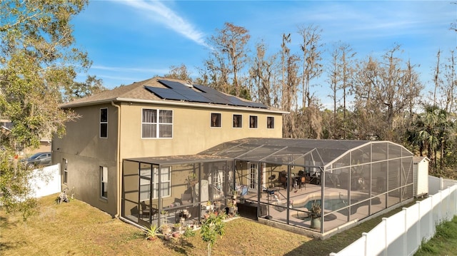 rear view of property featuring solar panels, a patio area, glass enclosure, and a yard