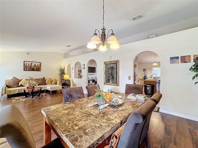 dining room with vaulted ceiling, hardwood / wood-style floors, a textured ceiling, and a chandelier