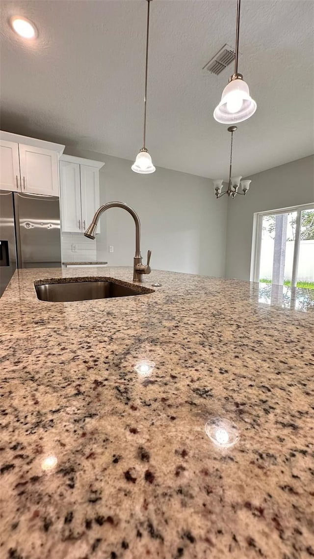 kitchen featuring sink, white cabinets, a textured ceiling, and hanging light fixtures