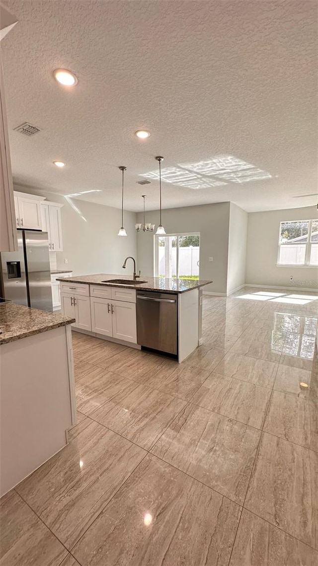 kitchen with stainless steel appliances, a center island with sink, white cabinetry, and pendant lighting