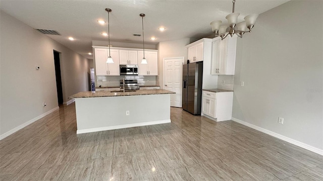 kitchen with stainless steel appliances, an island with sink, dark stone counters, pendant lighting, and white cabinetry