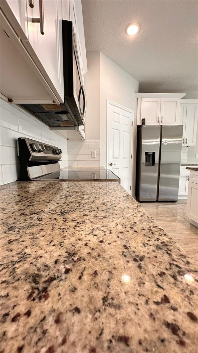 kitchen with appliances with stainless steel finishes, a textured ceiling, light stone counters, white cabinets, and backsplash