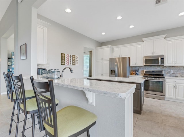 kitchen featuring white cabinetry, decorative backsplash, light stone countertops, and appliances with stainless steel finishes