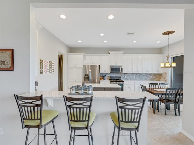 kitchen featuring a breakfast bar, decorative light fixtures, stainless steel appliances, decorative backsplash, and white cabinets