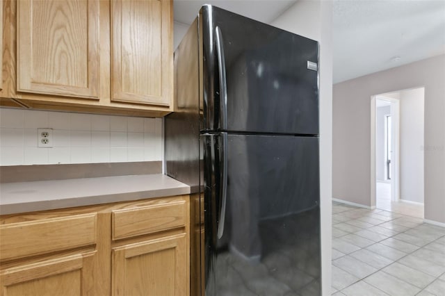 kitchen with black fridge, light tile patterned flooring, light brown cabinetry, and backsplash