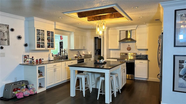 kitchen with wall chimney exhaust hood, stainless steel electric stove, a kitchen island, backsplash, and white cabinetry