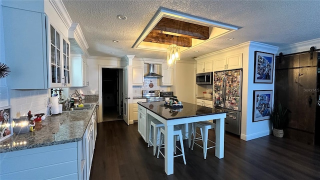 kitchen with wall chimney exhaust hood, a kitchen island, a barn door, white cabinetry, and appliances with stainless steel finishes