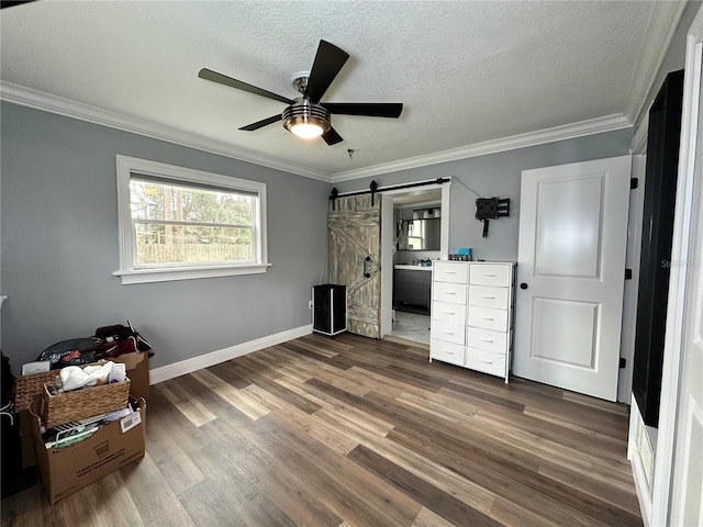 unfurnished bedroom featuring ensuite bath, a barn door, crown molding, ceiling fan, and a textured ceiling