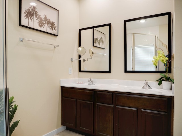 bathroom featuring double vanity, a stall shower, baseboards, and a sink