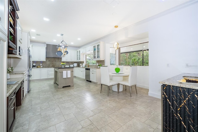 kitchen featuring wall chimney range hood, pendant lighting, white cabinets, and stainless steel appliances