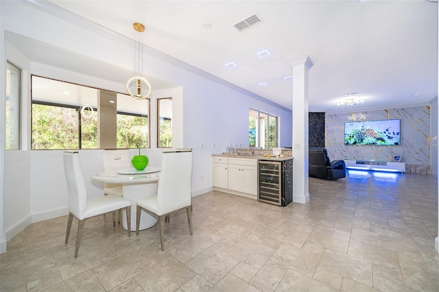 interior space featuring beverage cooler, decorative light fixtures, a kitchen bar, white cabinetry, and decorative columns