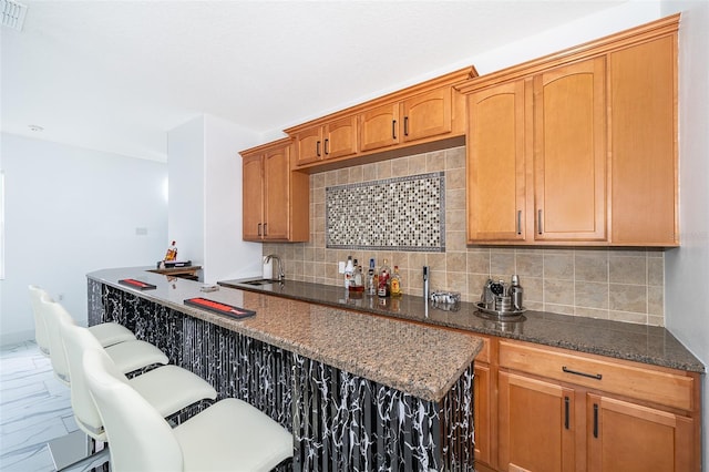 kitchen featuring a kitchen breakfast bar, sink, backsplash, and dark stone countertops