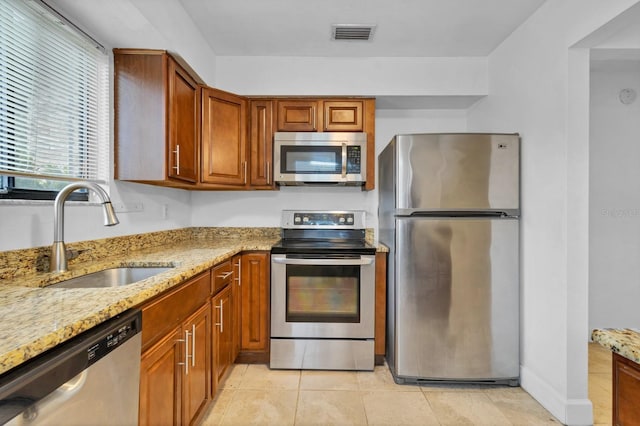 kitchen with light tile patterned floors, appliances with stainless steel finishes, light stone counters, and sink