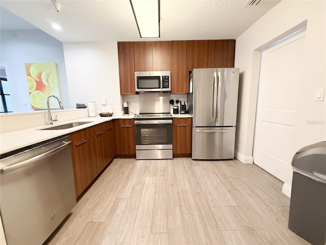 kitchen with sink, stainless steel appliances, a textured ceiling, and light wood-type flooring