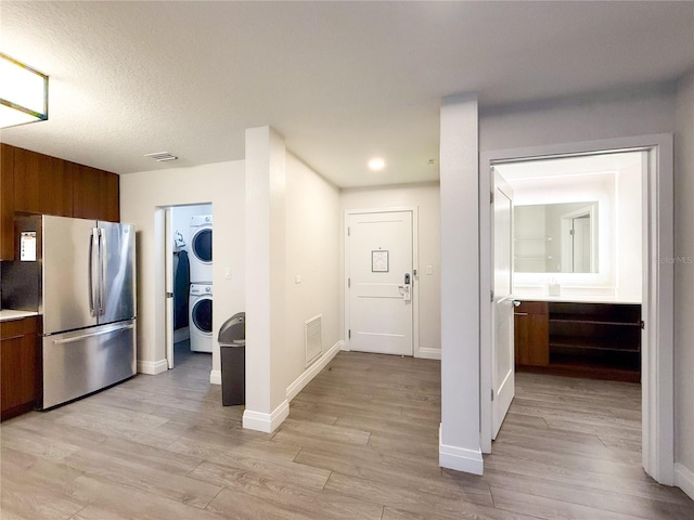 interior space with stacked washer and dryer, stainless steel refrigerator, and light hardwood / wood-style floors