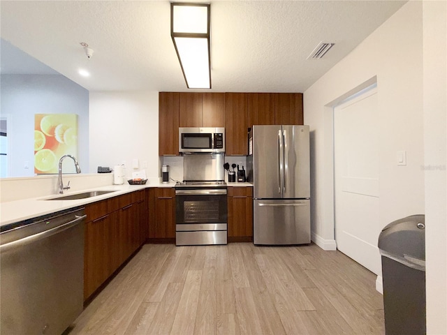 kitchen with appliances with stainless steel finishes, sink, a textured ceiling, and light hardwood / wood-style floors