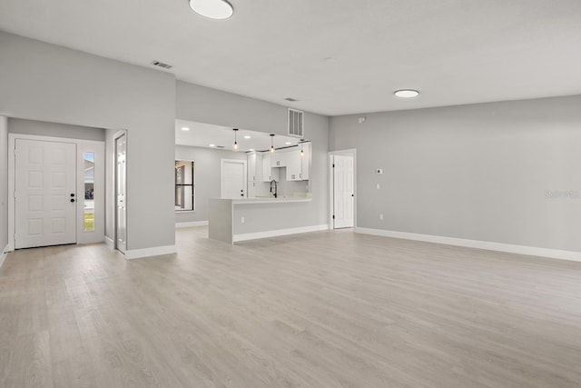 unfurnished living room featuring lofted ceiling, sink, and light hardwood / wood-style flooring